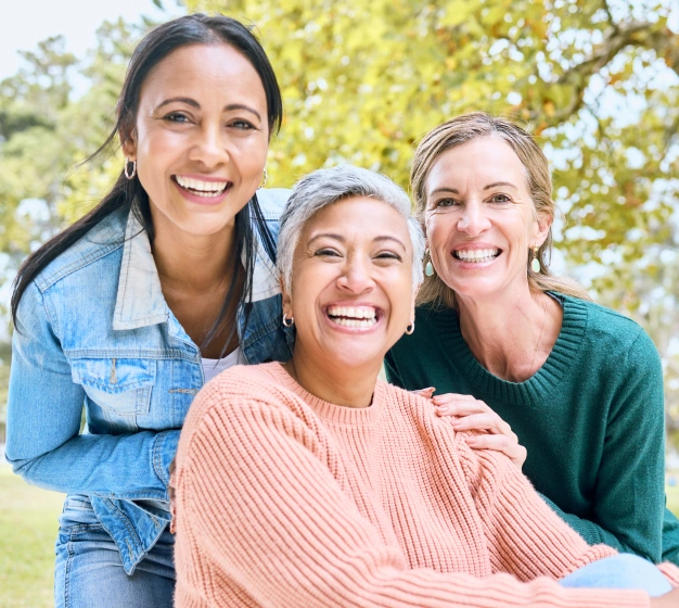 Three women smiling together outdoors with healthy smiles