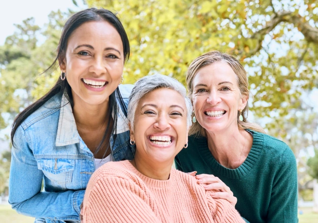 Three women smiling together outdoors with healthy smiles