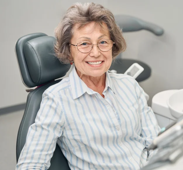 Smiling older woman sitting in a dental chair during a dental visit.